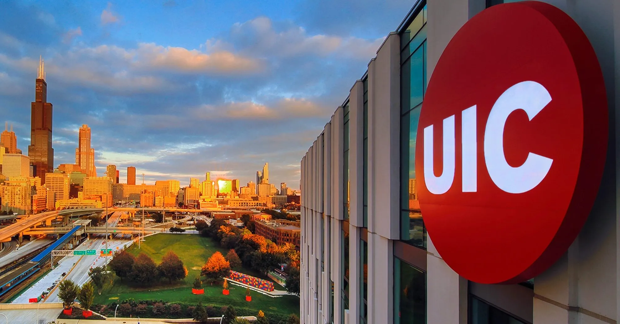 UIC sign on a campus building overlooking the Chicago skyline at sunset.